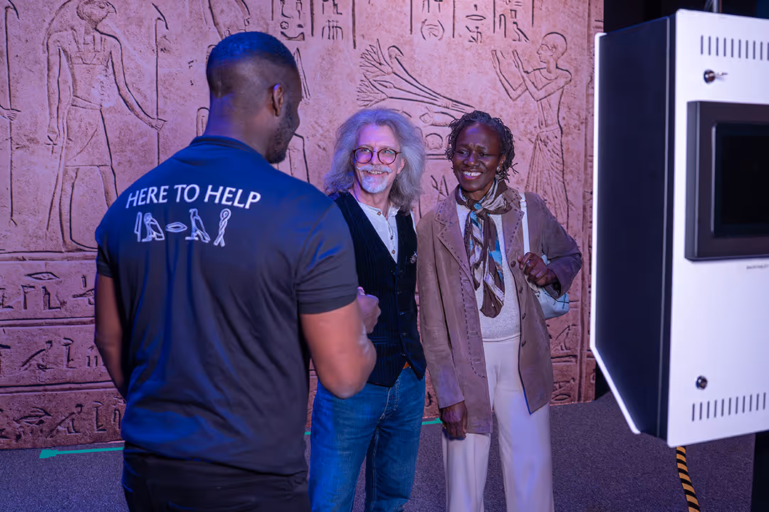 Two people smiling, posing for photo with an assistant providing a guided tour through Ramses The Exhibition