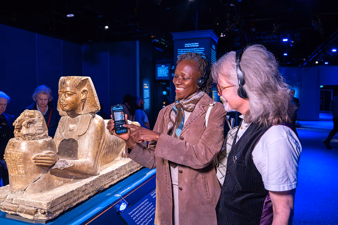 Two museum visitors with headphones are listening to the audio guide for Ramses The Exhibition.