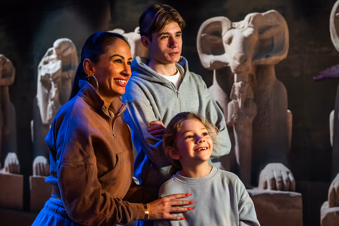 A smiling woman with two kids is looking at ancient stone statues in Ramses The Exhibition.