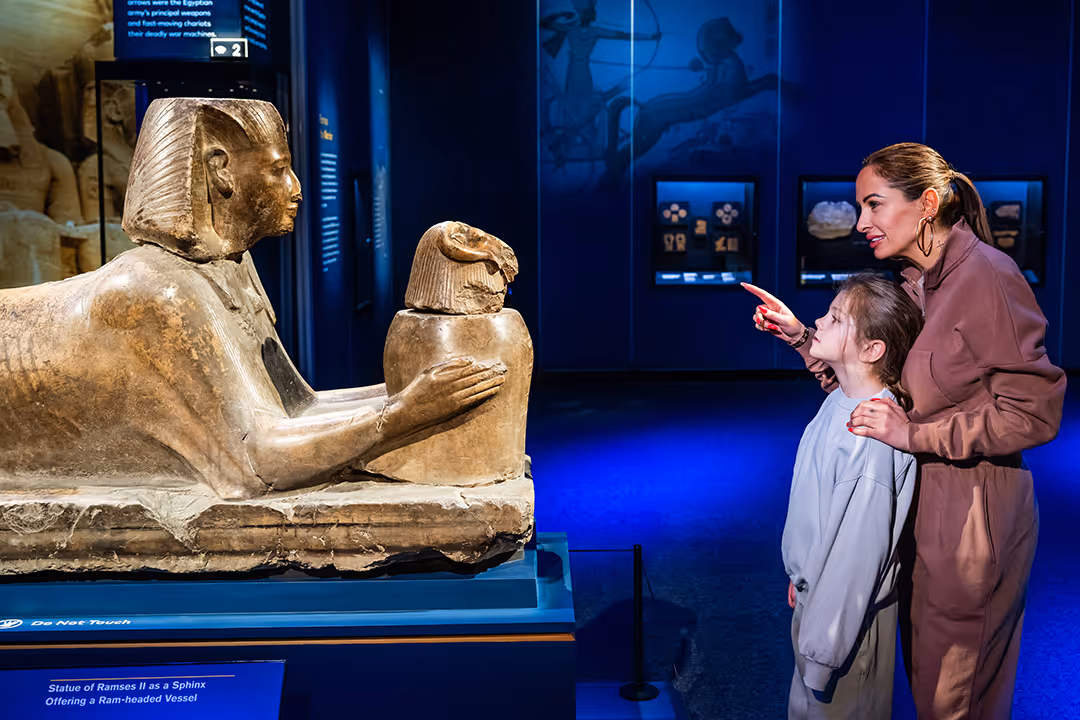 Woman and child are observing an ancient Egyptian sphinx statue in the Ramses Exhibition.