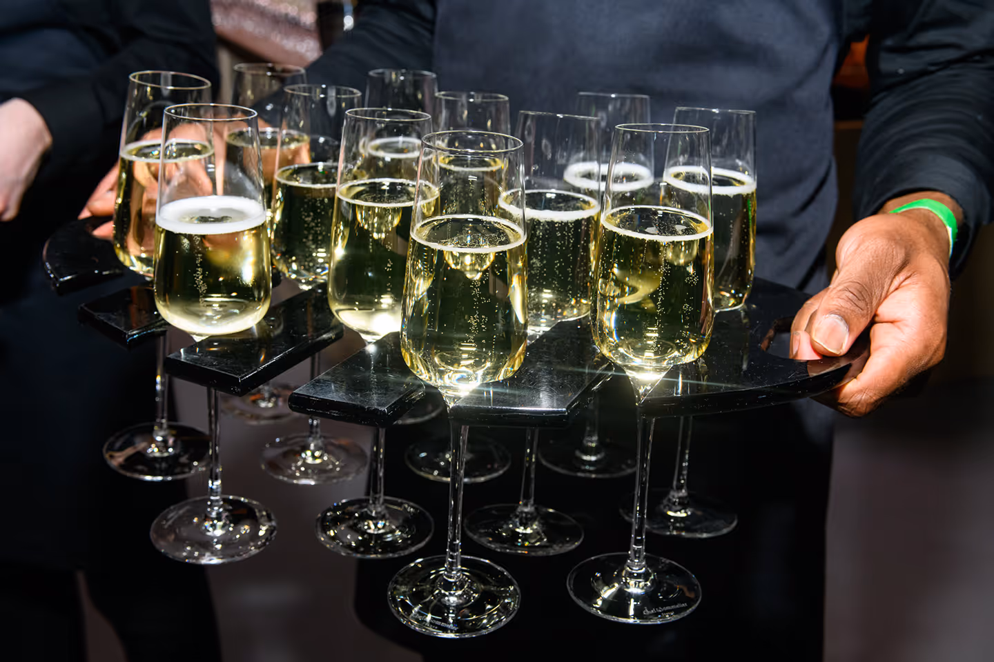 Person holding a tray with multiple champagne flutes filled with sparkling wine.