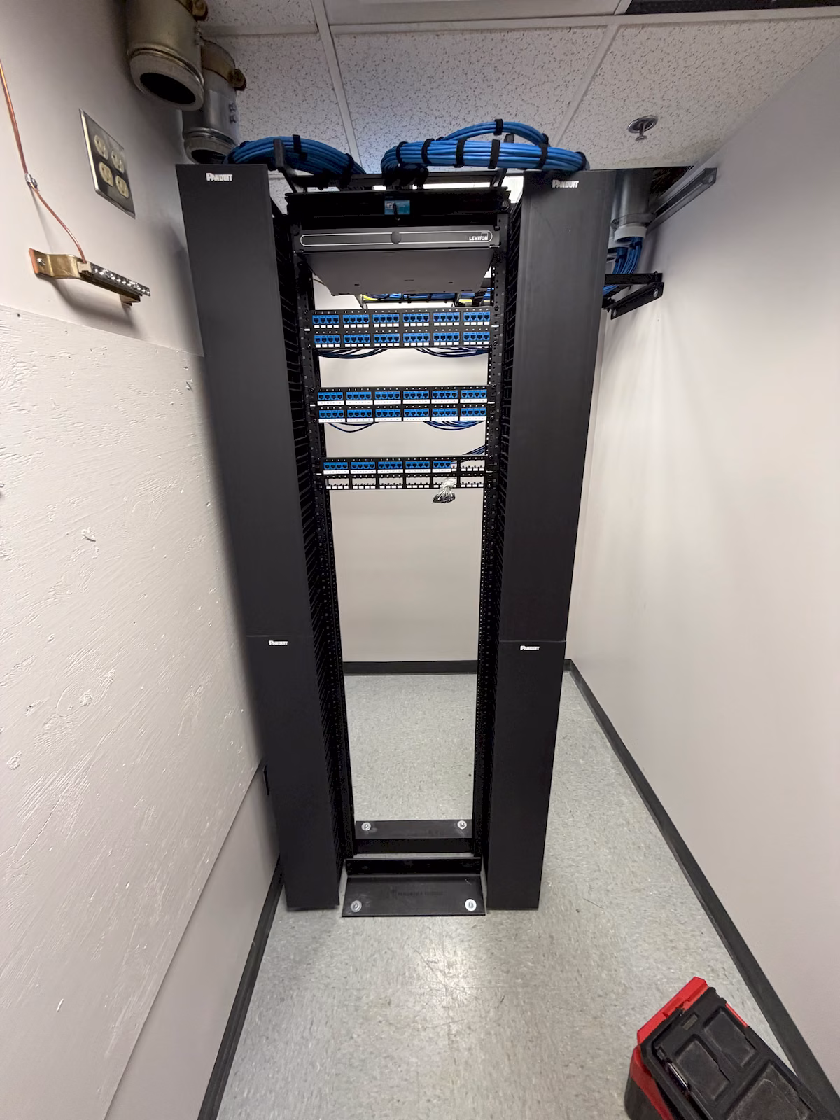 Blue network cable bundles secured to an overhead ladder tray above the equipment rack.