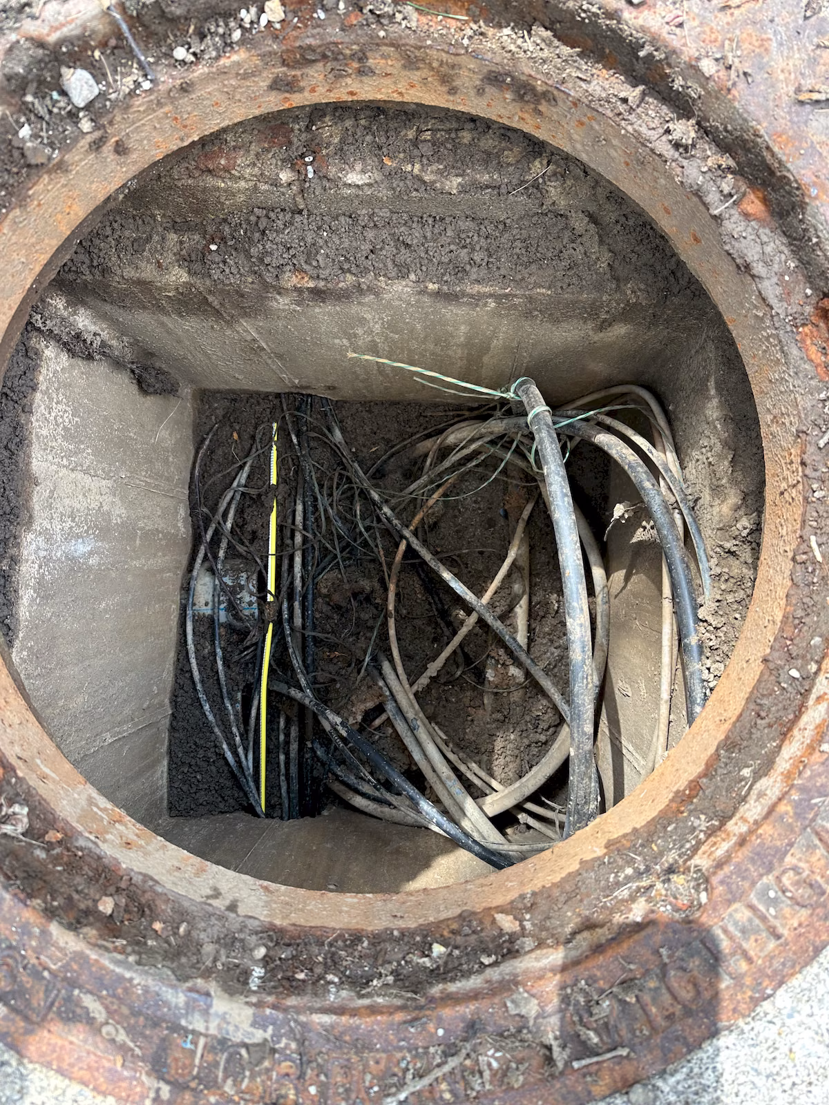 Interior of an underground communications manhole containing existing cables and newly routed yellow fiber cable.
