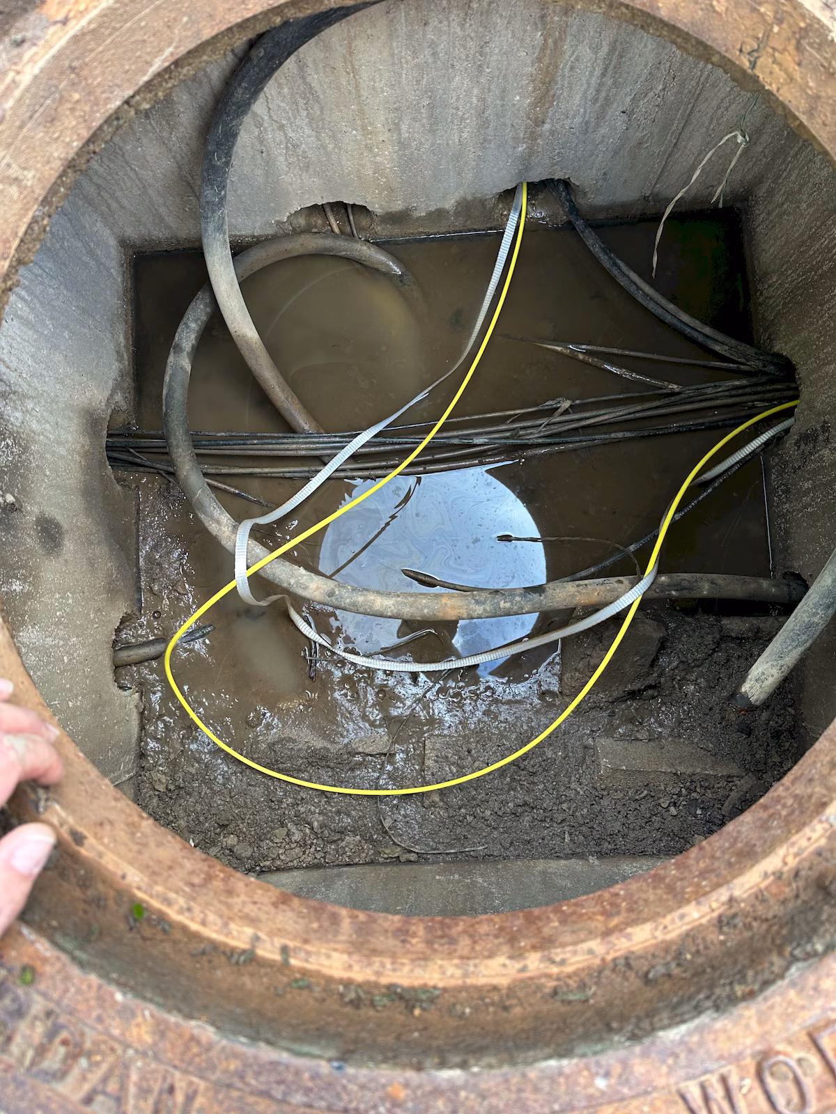 Micro-armored fiber cable routed through a water-filled underground communications vault with existing utility cables.