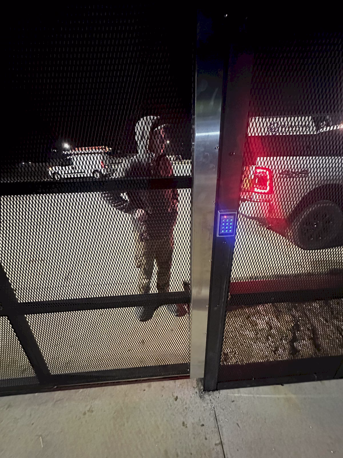 Access control keypad being tested on a secured exterior metal gate at night.