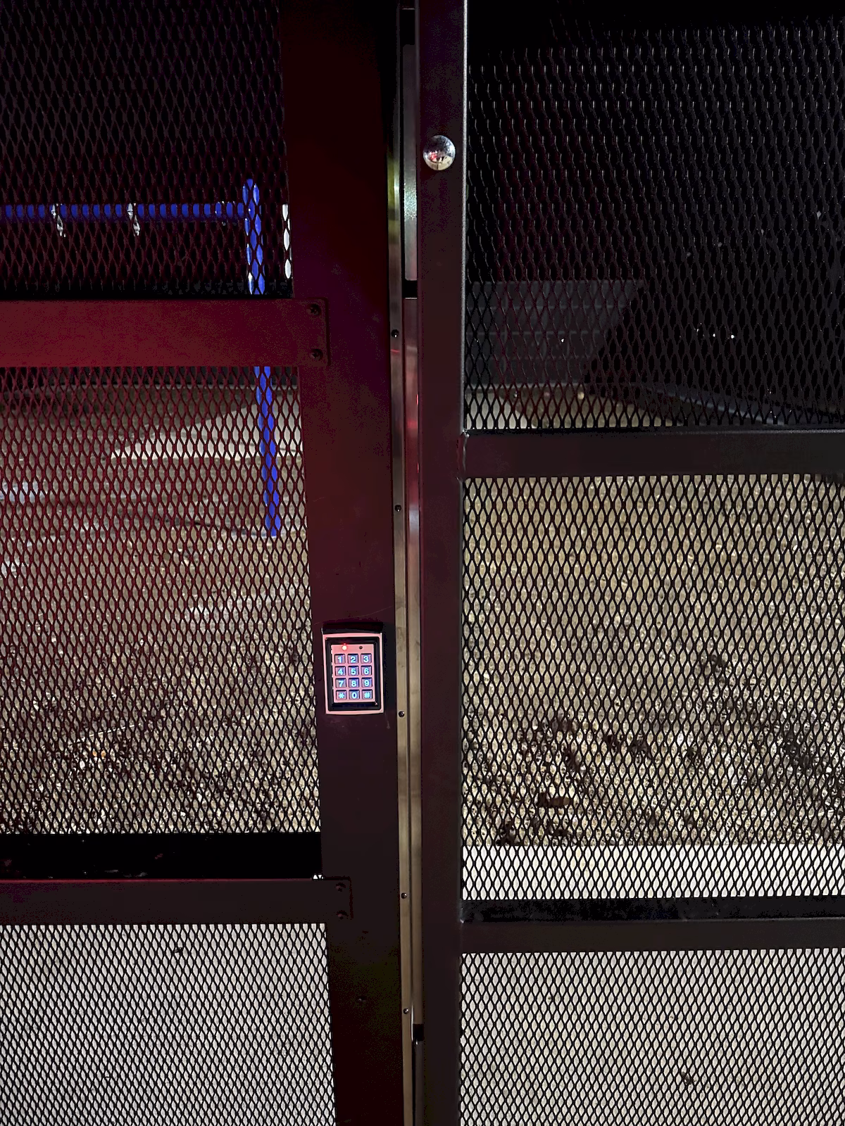 Close view of an illuminated access keypad beside the full-length magnetic lock on a metal gate.