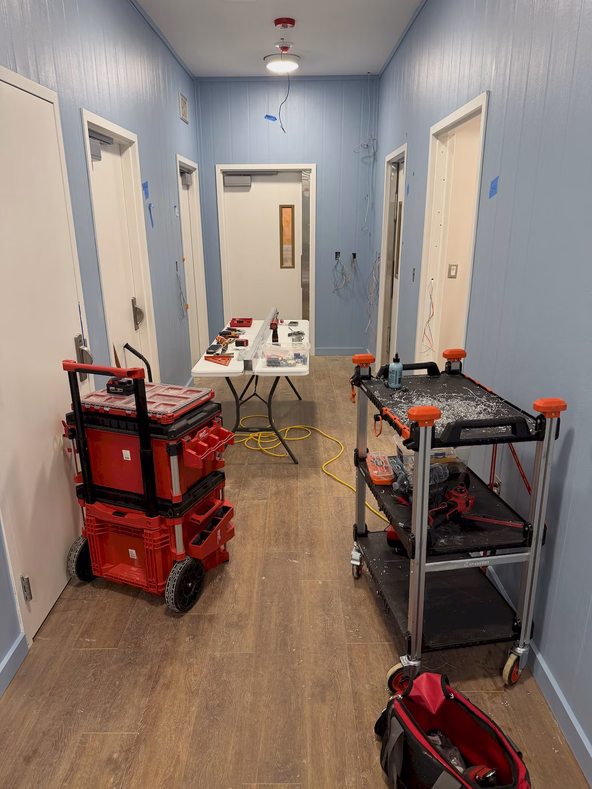 Commercial hallway worksite during installation of full-length electromagnetic locks on multiple doors.