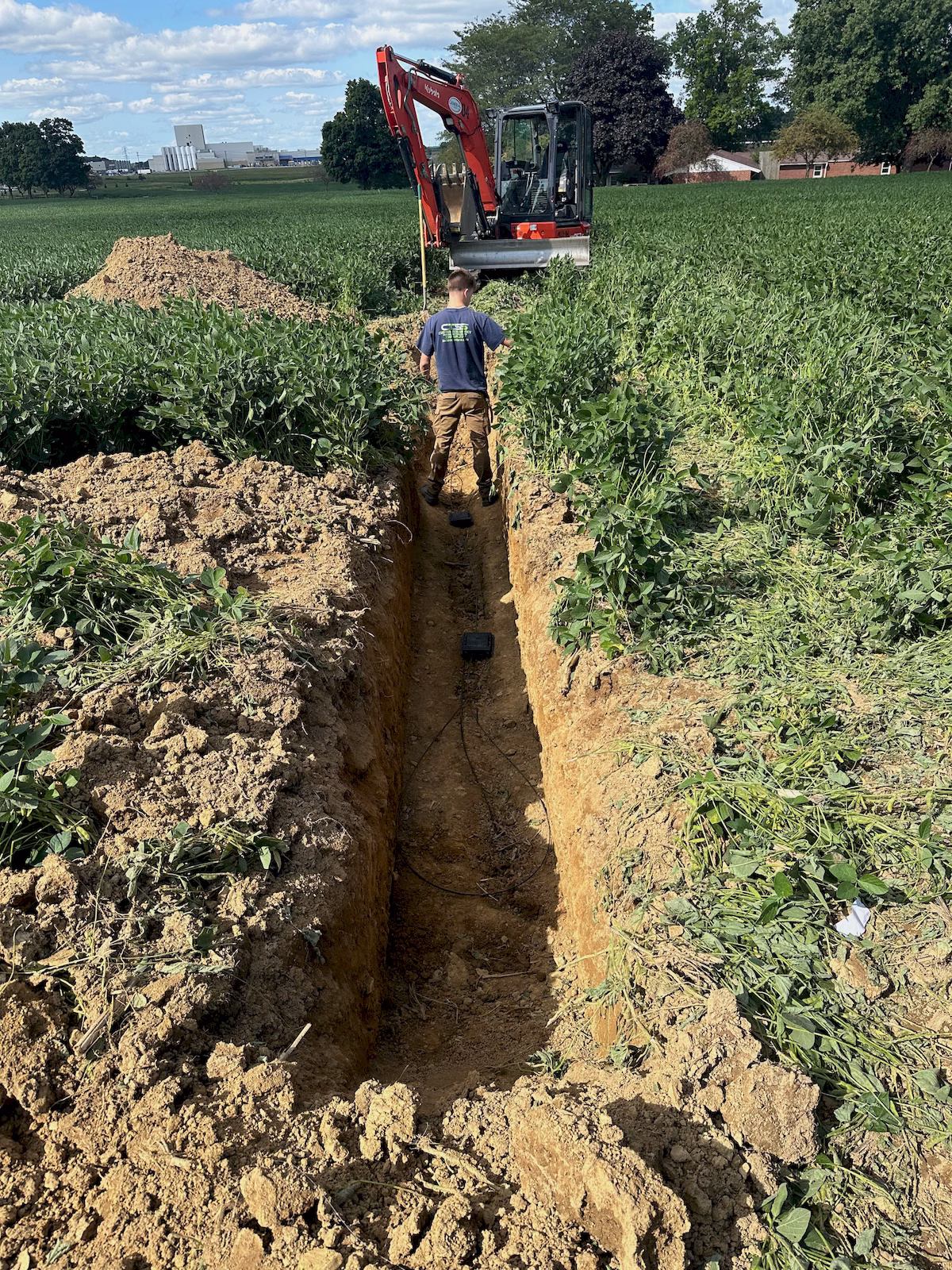 Technician working inside an excavated field trench containing underground fiber cable and splice closures.