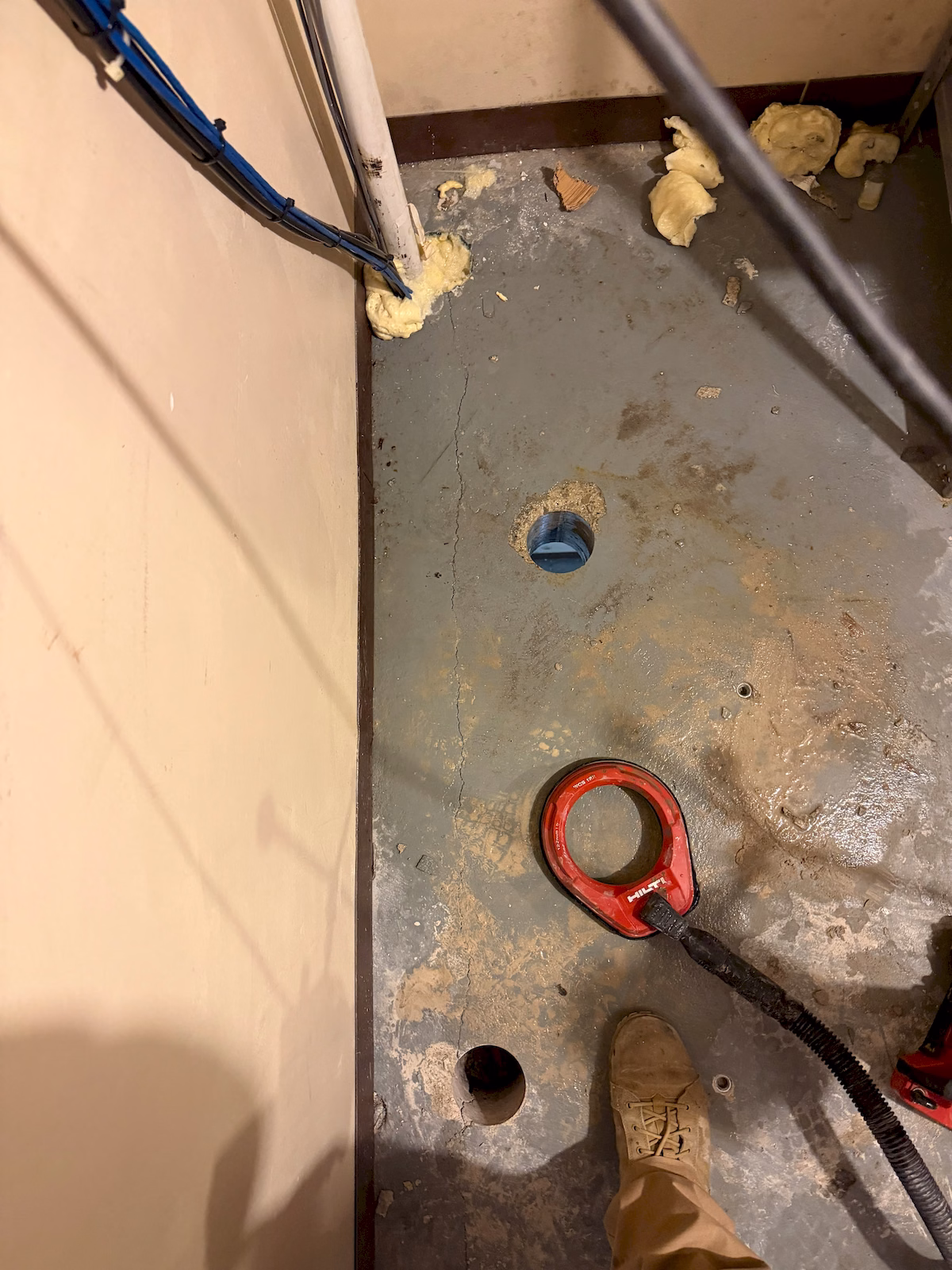 Multiple core-drilled openings through a concrete floor prepared for vertical low-voltage cable routing.