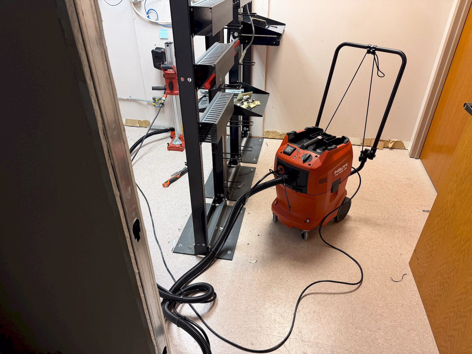 Dust extraction equipment connected to a concrete core-drilling setup inside a communications room.