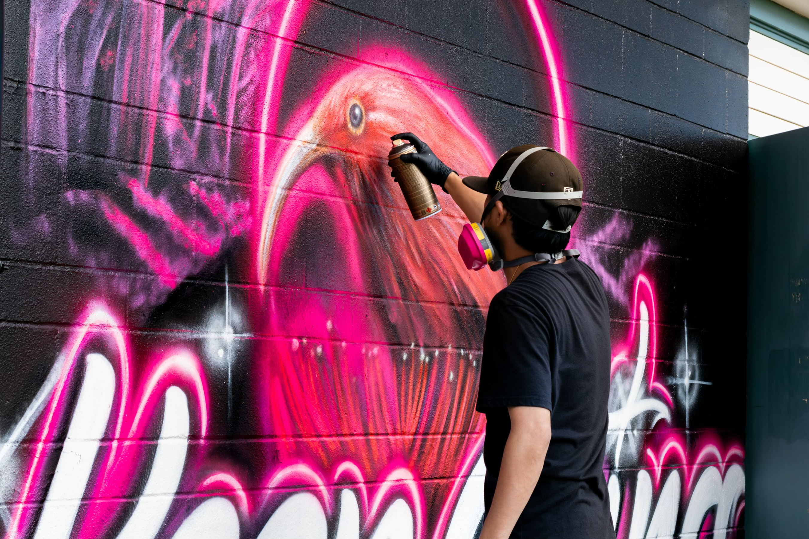 Trysen Kaneshige spray-painting an ʻiʻiwi on the Keep Going mural at Kōloa Elementary School during Spectra Fest