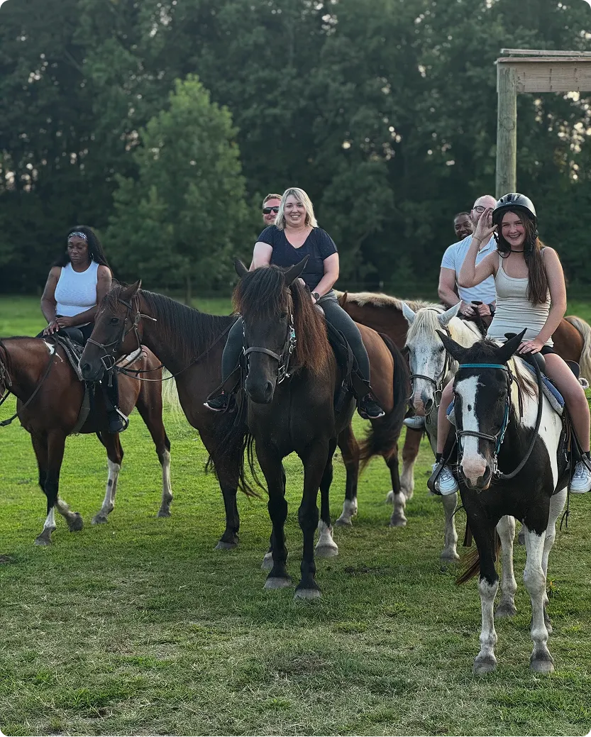 Smiling riders on horseback approach across a green field, with a girl waving from a black-and-white pinto.