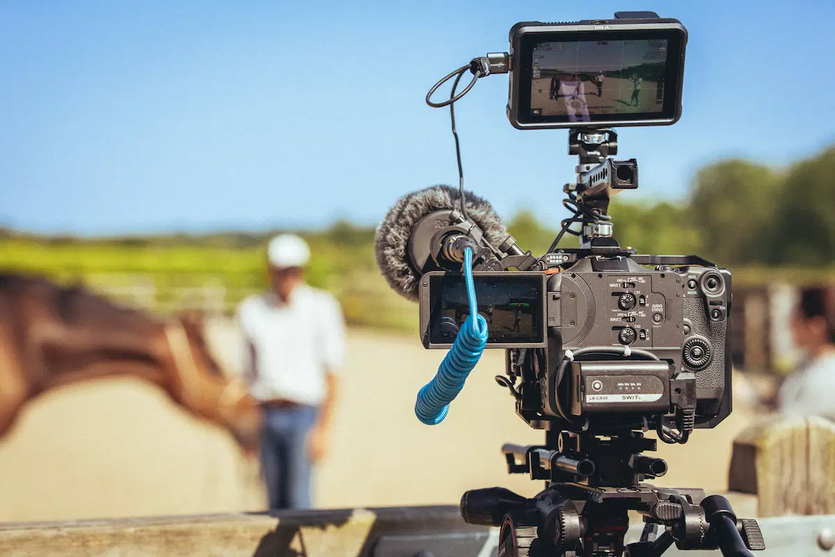 Professional video camera with external microphone set up outdoors to film an equestrian scene
