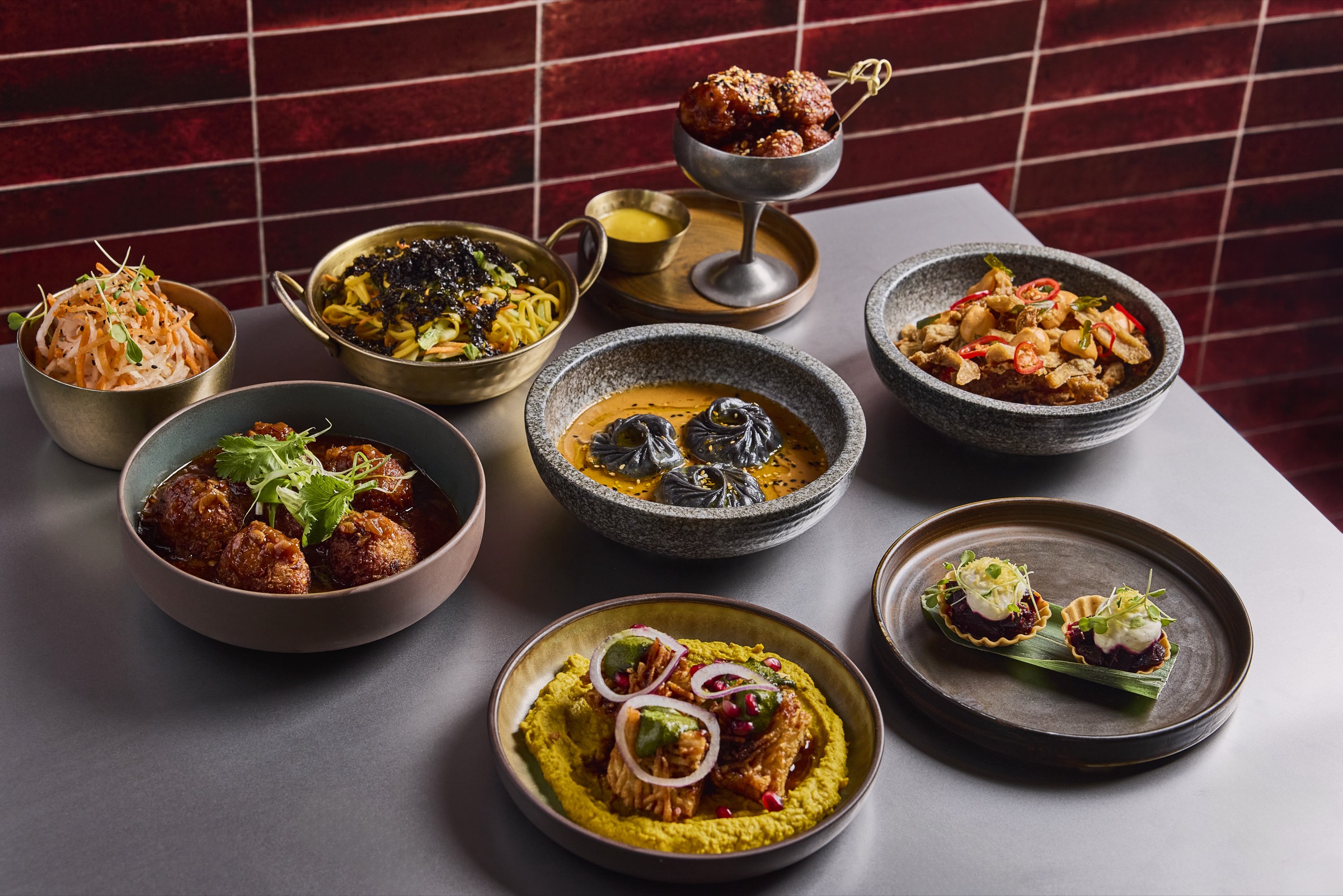 A spread of Tangra's Indo-Chinese sharing dishes on a steel table against a deep red tiled wall