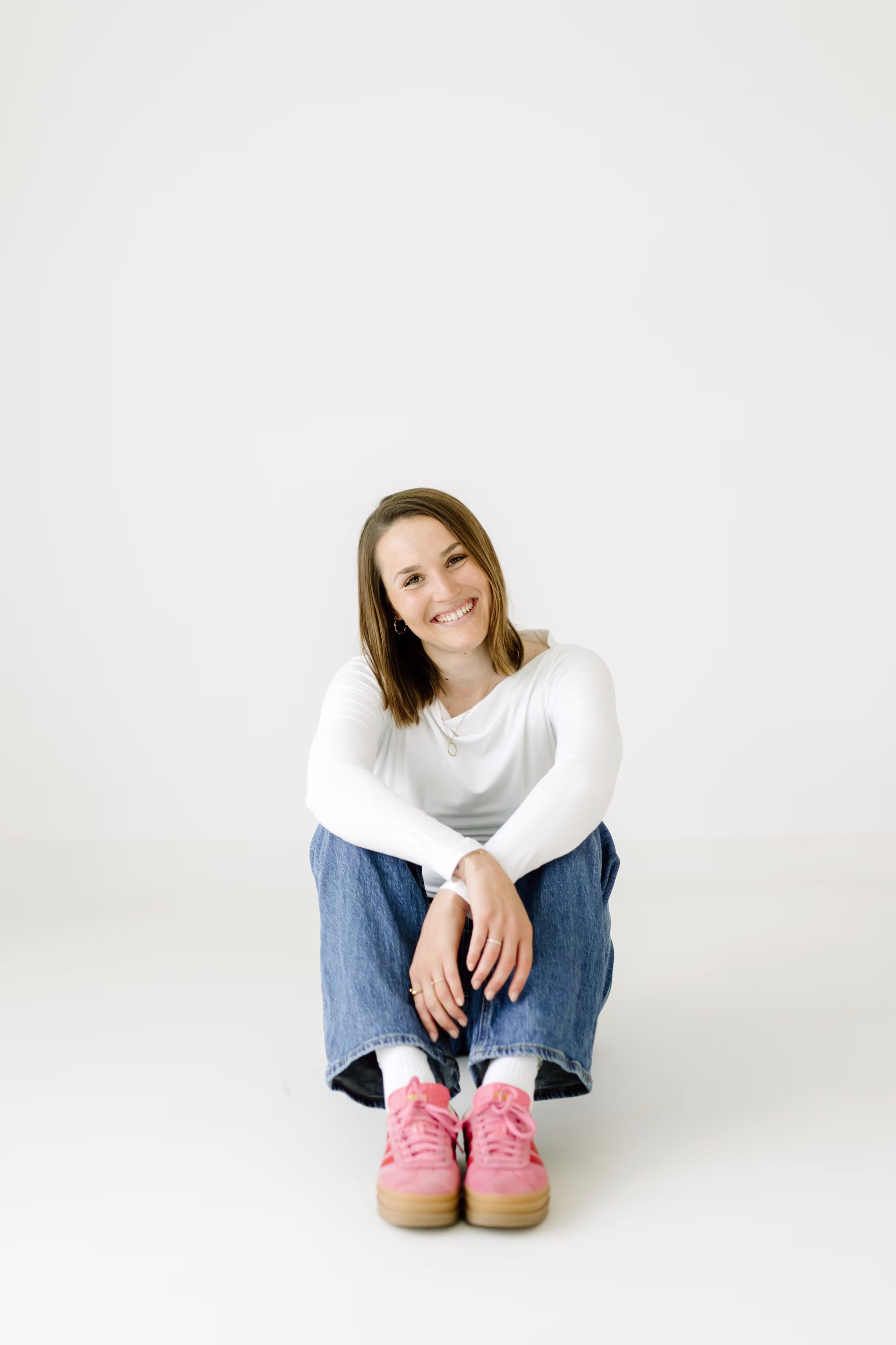 Hanna Blank, Sportpsychologin, sitzt lächelnd auf hellem Boden.