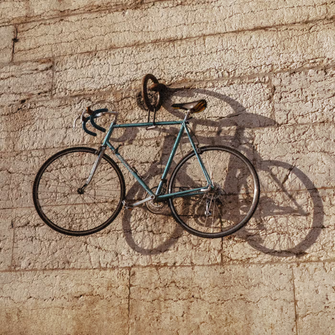 Ein blaues Rennrad hängt mit einem Schloss an einer hellen Steinwand und wirft Schatten.