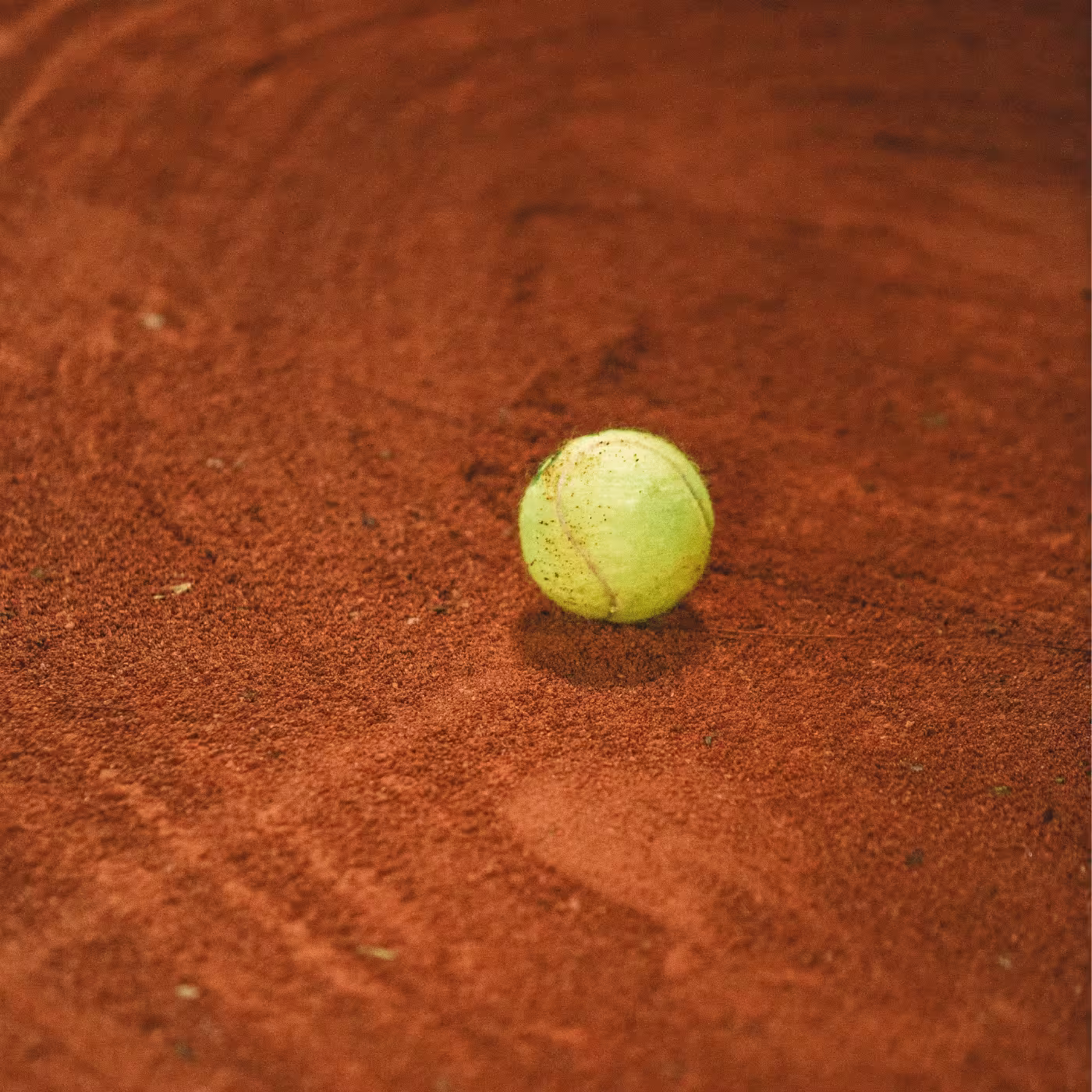 Ein Tennisschläger auf rotem Sandplatz mit Linien im Hintergrund.