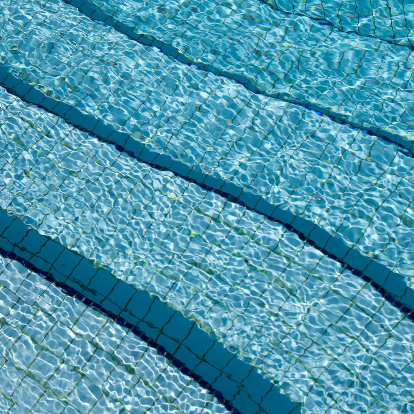 Nahaufnahme von Poolstufen mit blauem Wasser und Fliesen, die Lichtreflexionen zeigen.