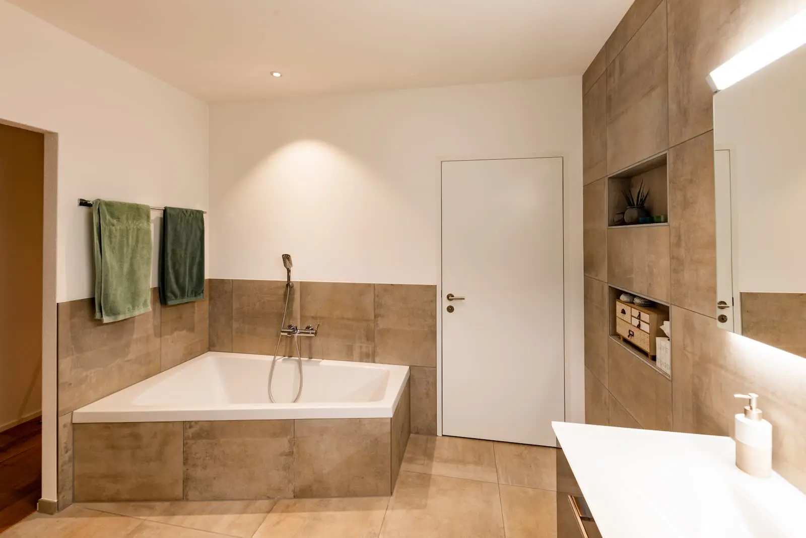 Badezimmer im Einfamilienhaus Gansingen mit Eckbadewanne, Sichtbeton-Optik und wandintegrierten Ablagenischen