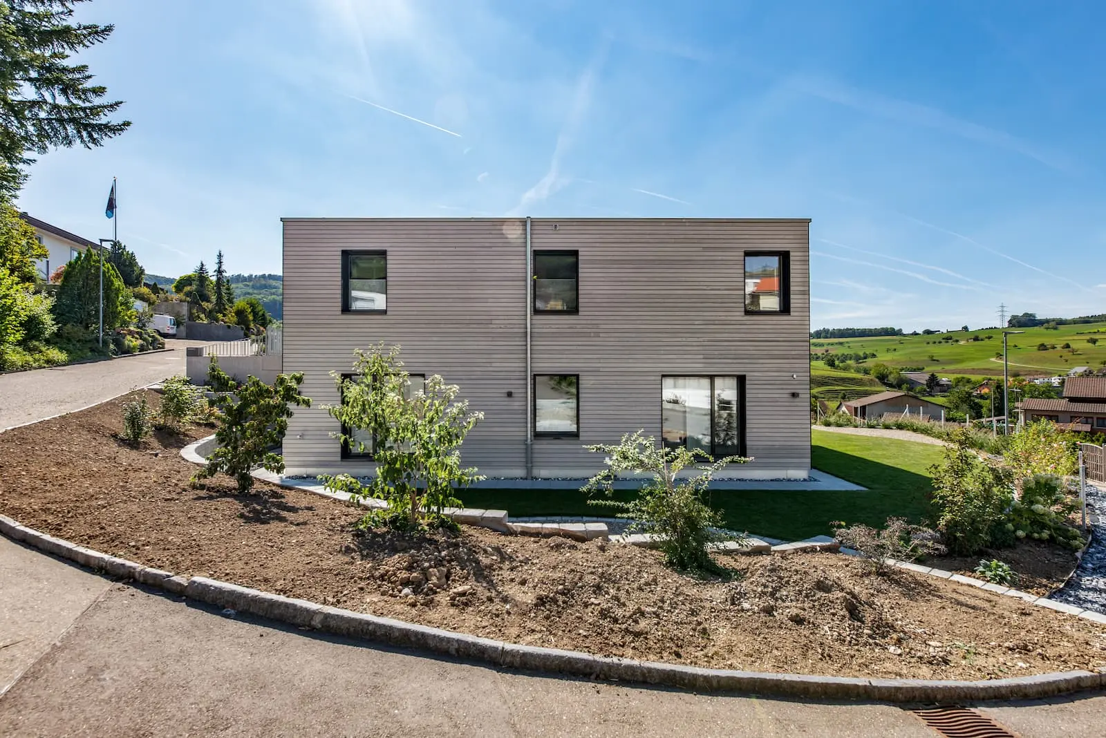 Gartenansicht des Einfamilienhauses in Gansingen mit Holzfassade, gedeckter Terrasse und Sichtbetonanbau