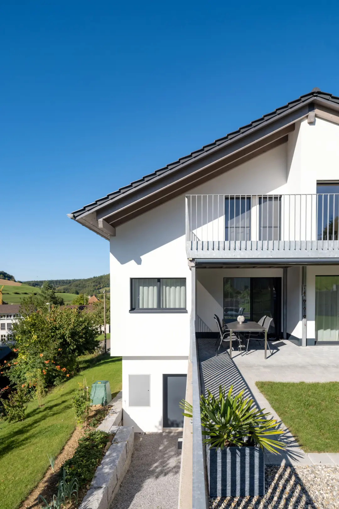 Seitenansicht des Einfamilienhauses in Sulz mit gedeckter Terrasse und Gartenbereich in Hanglage