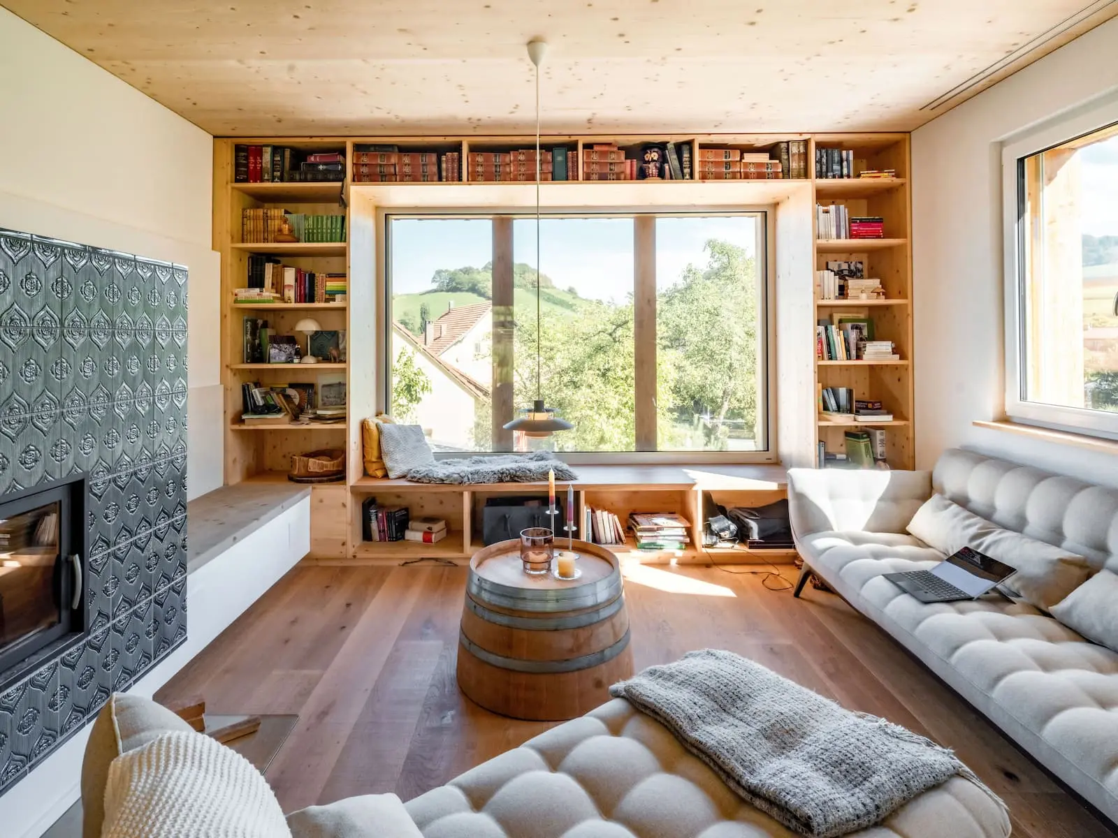 Wohnraum mit raumhohem Panoramafenster, Bücherregal in Holz und Kachelofen im Einfamilienhaus in Mandach.
