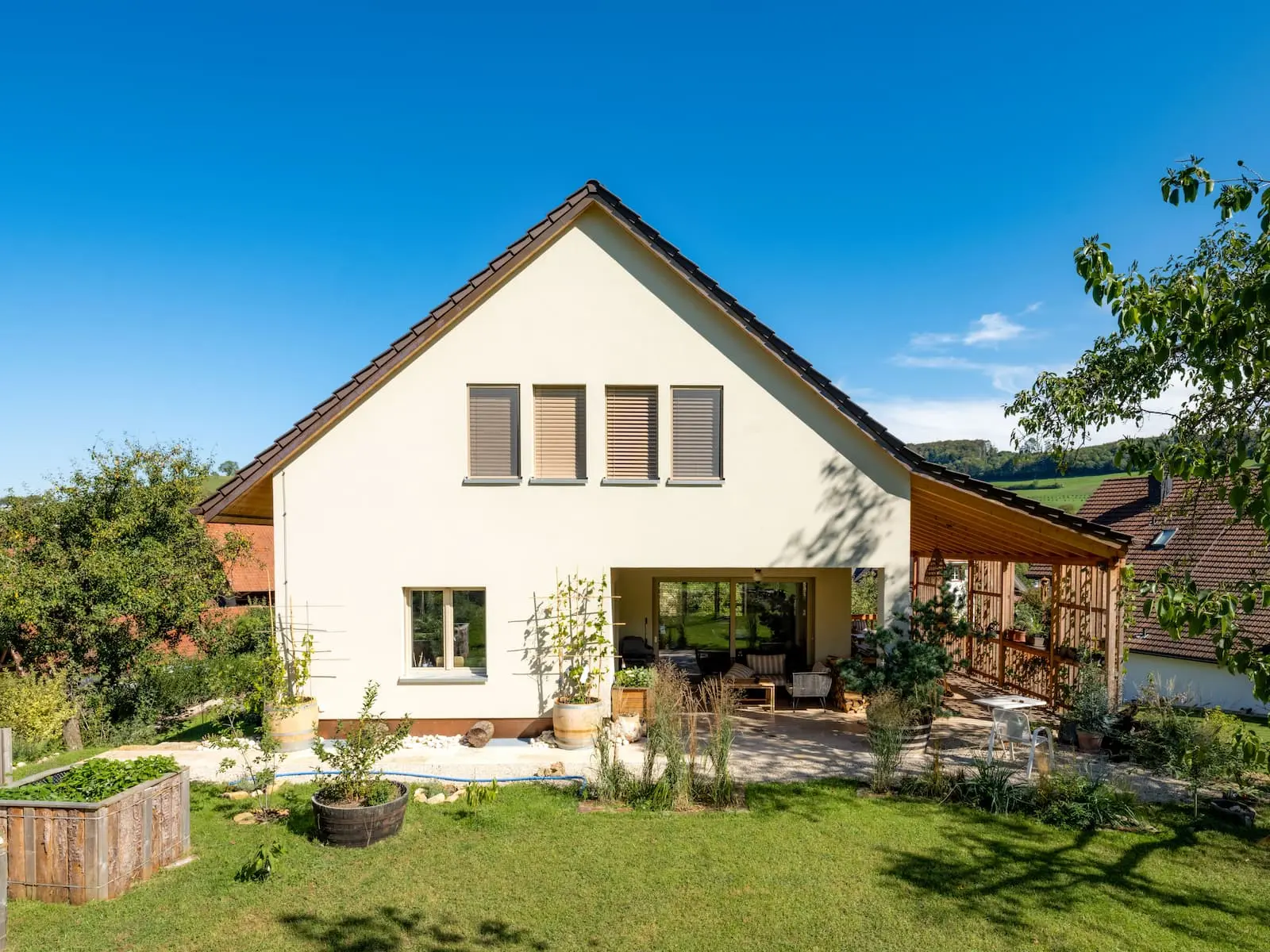 Giebelfassade des Einfamilienhauses in Mandach mit verputzter Wand, gedecktem Sitzplatz und Rankgerüst aus Holz.