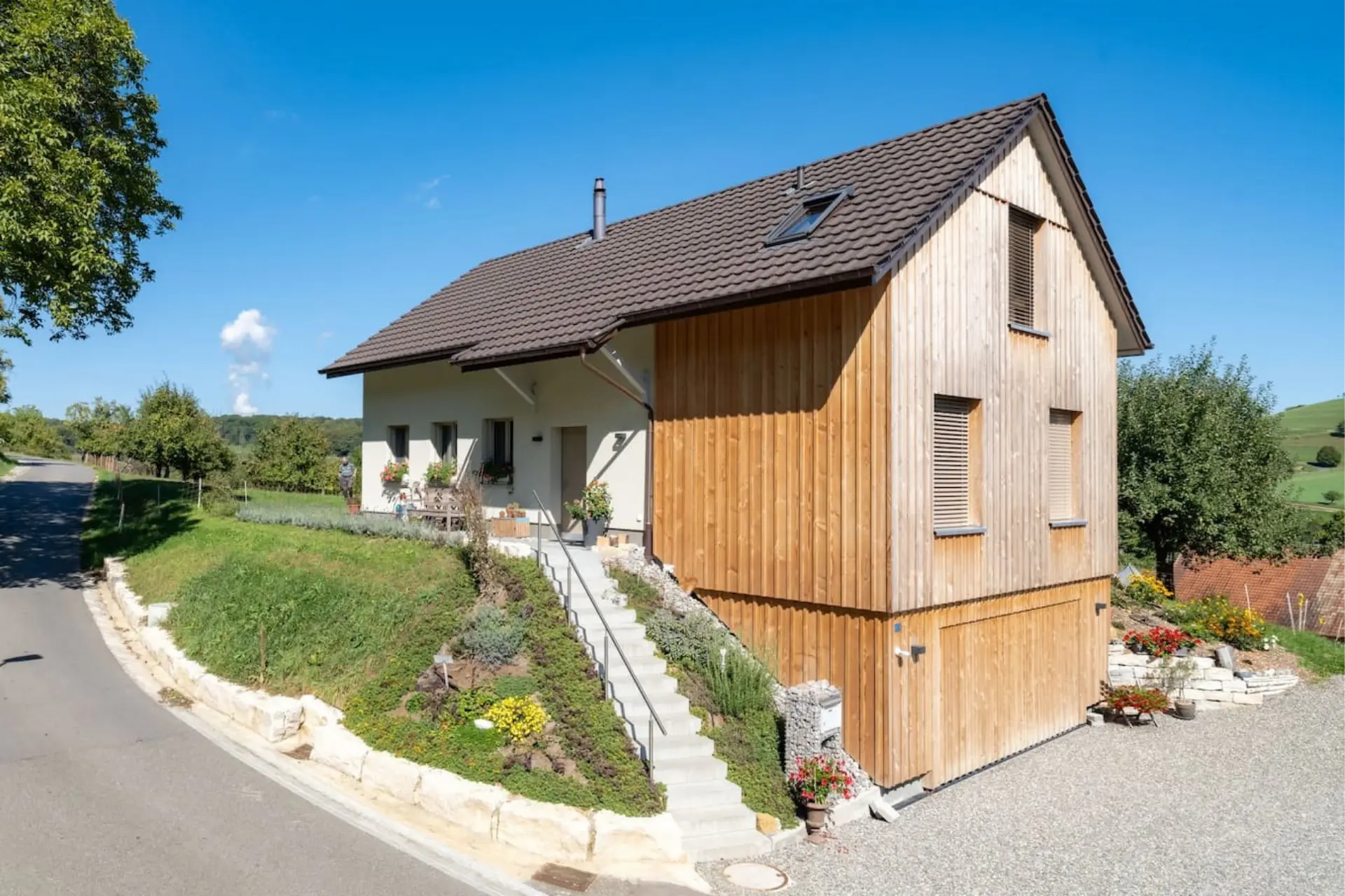 Einfamilienhaus in Holzelementbauweise in Mandach mit verputzter Fassade, Holzverschalung am Anbau und Aussentreppe zum Hauseingang.