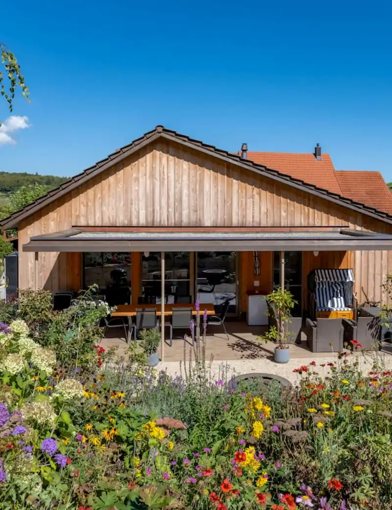 Dachaufstockung mit Terrasse, Garten mit bunten Blumen bei klarem blauem Himmel.