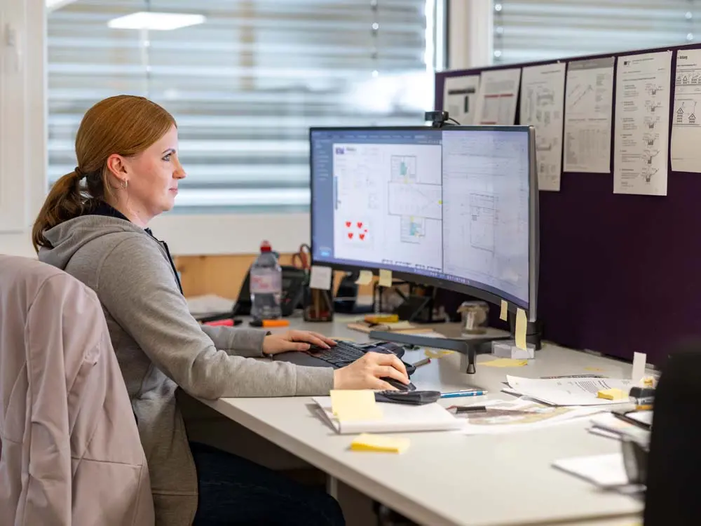 Cecile Heggli arbeitet konzentriert an einem grossen gebogenen Monitor an einem Schreibtisch im Büro.