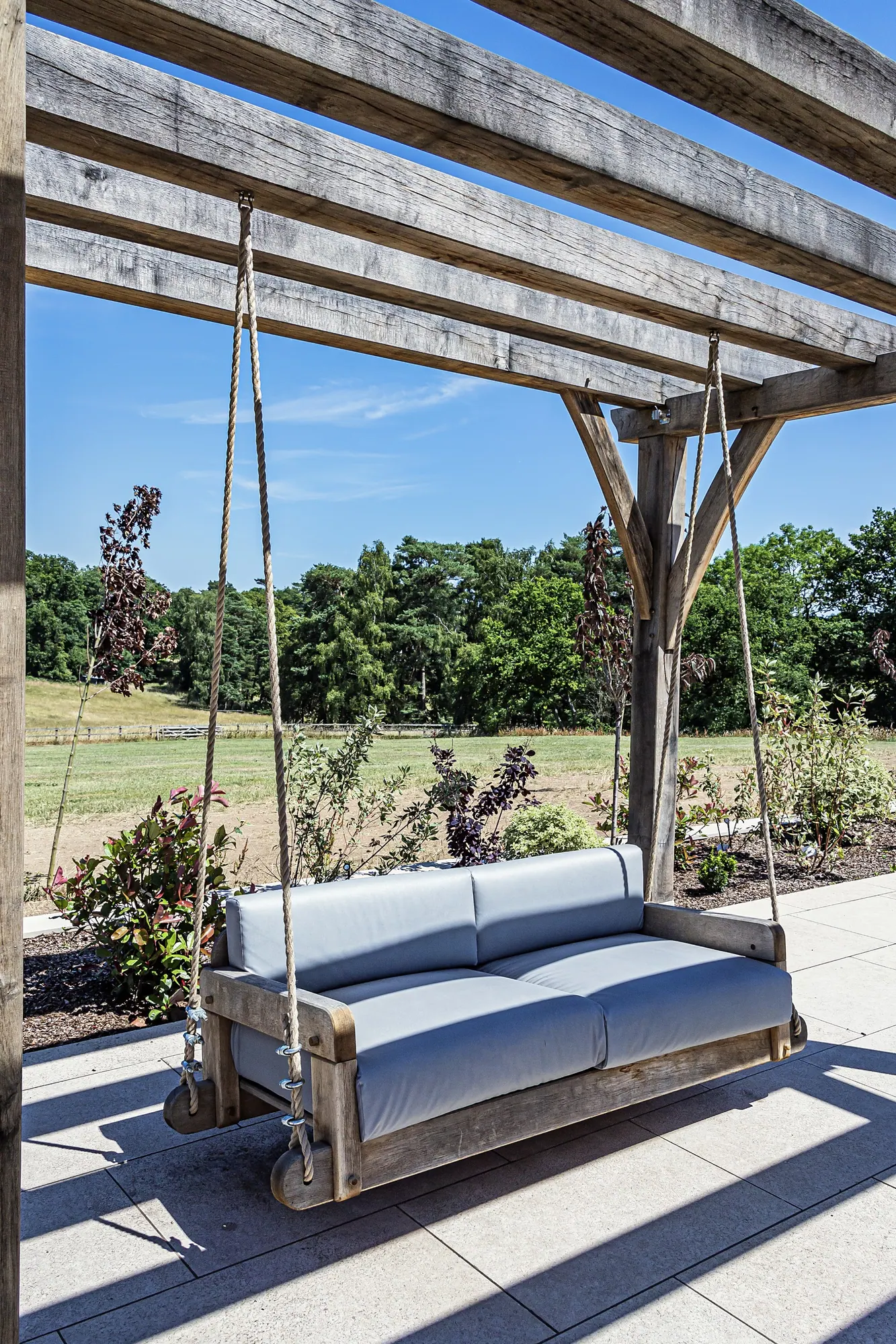 Hanging oak sofa on ropes under an oak pergola with braced posts, on a paved garden terrace at Ullenhall, Warwickshire