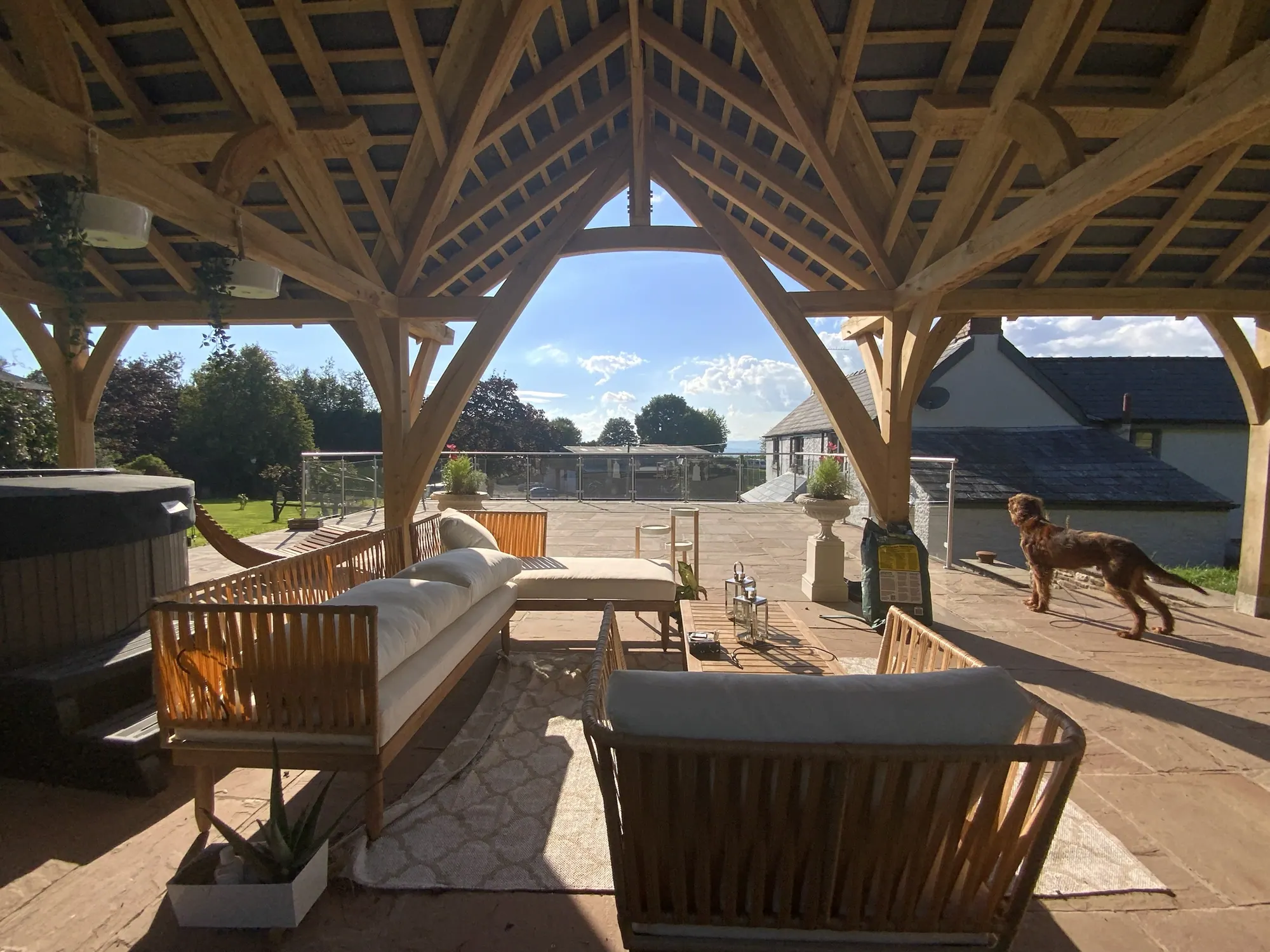 Looking out from under the oak garden pavilion at Devauden, the curved crucks framing the view across the terrace to the hills.