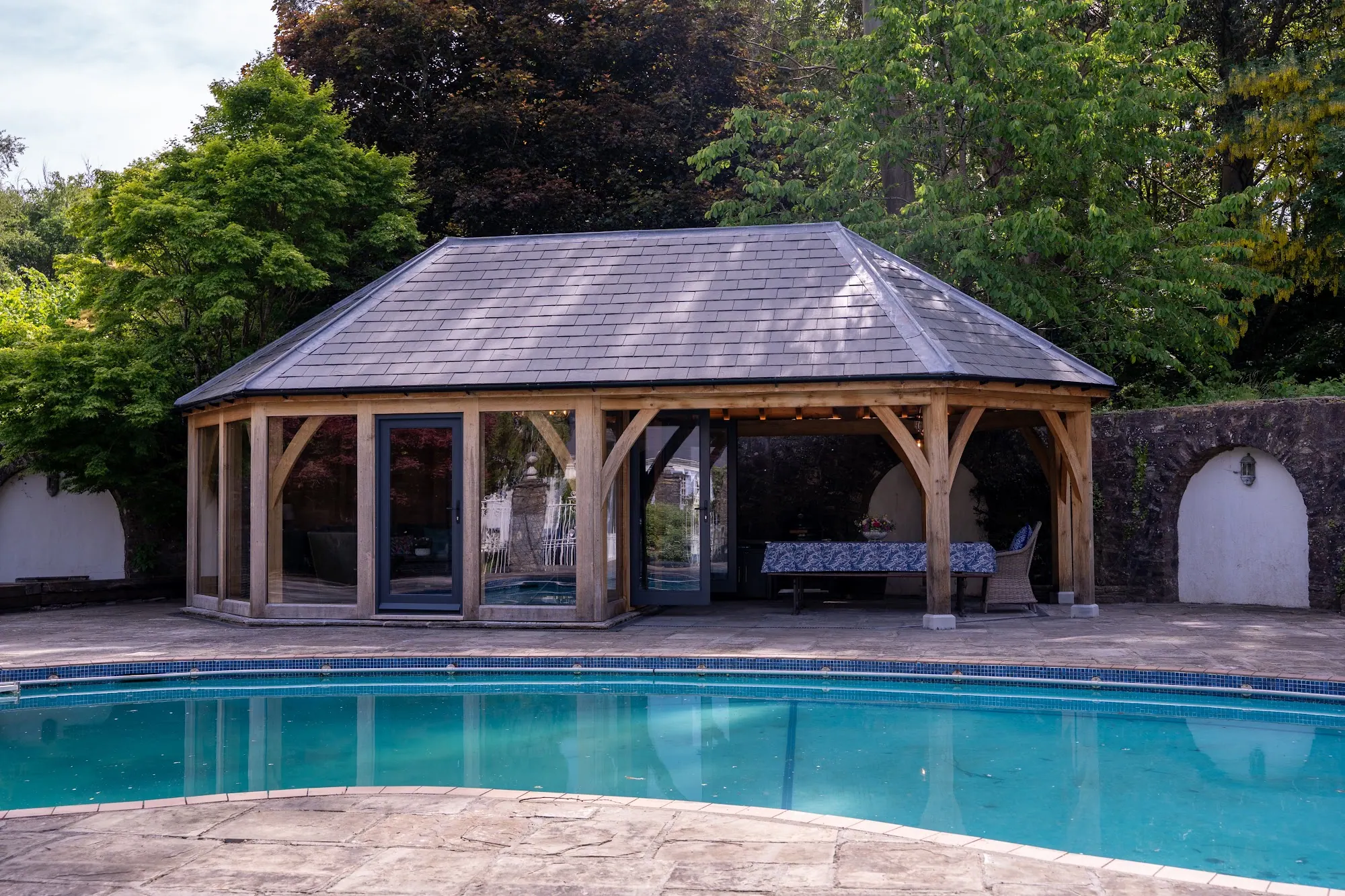 The pool house at Peterston-super-Ely beside the outdoor pool, a hipped roof over oak posts and glazed doors.