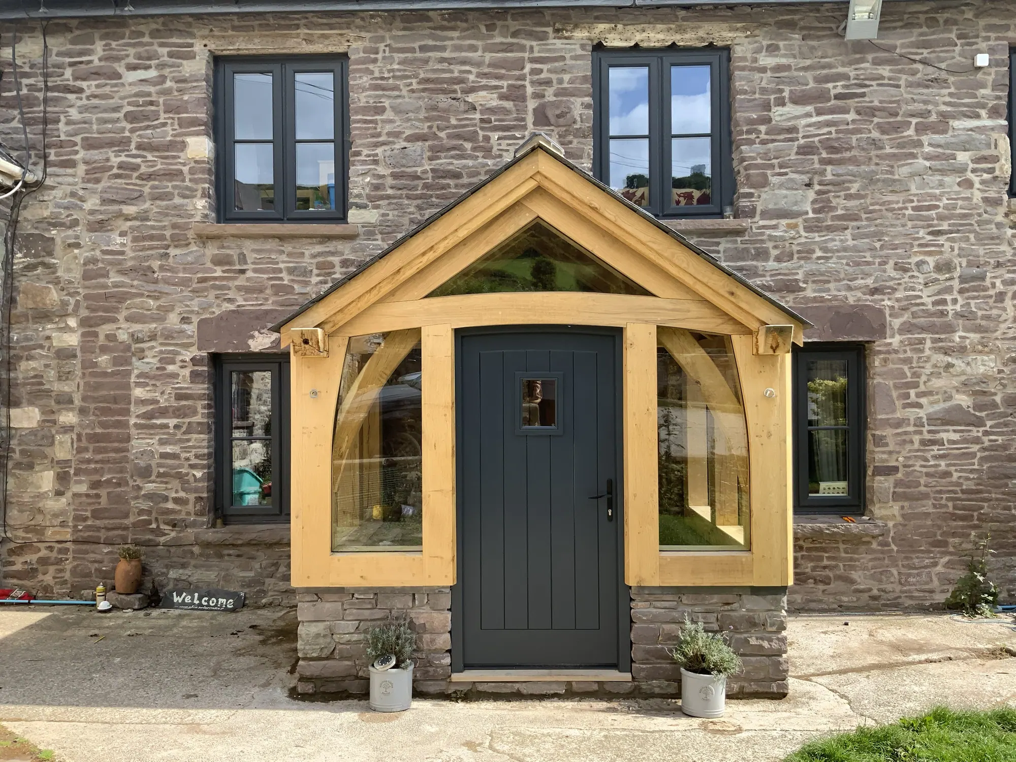 A glazed oak gable porch on a stone farmhouse at Llanbedr, near Crickhowell, with a curved tie beam and curved braces framing a dark front door