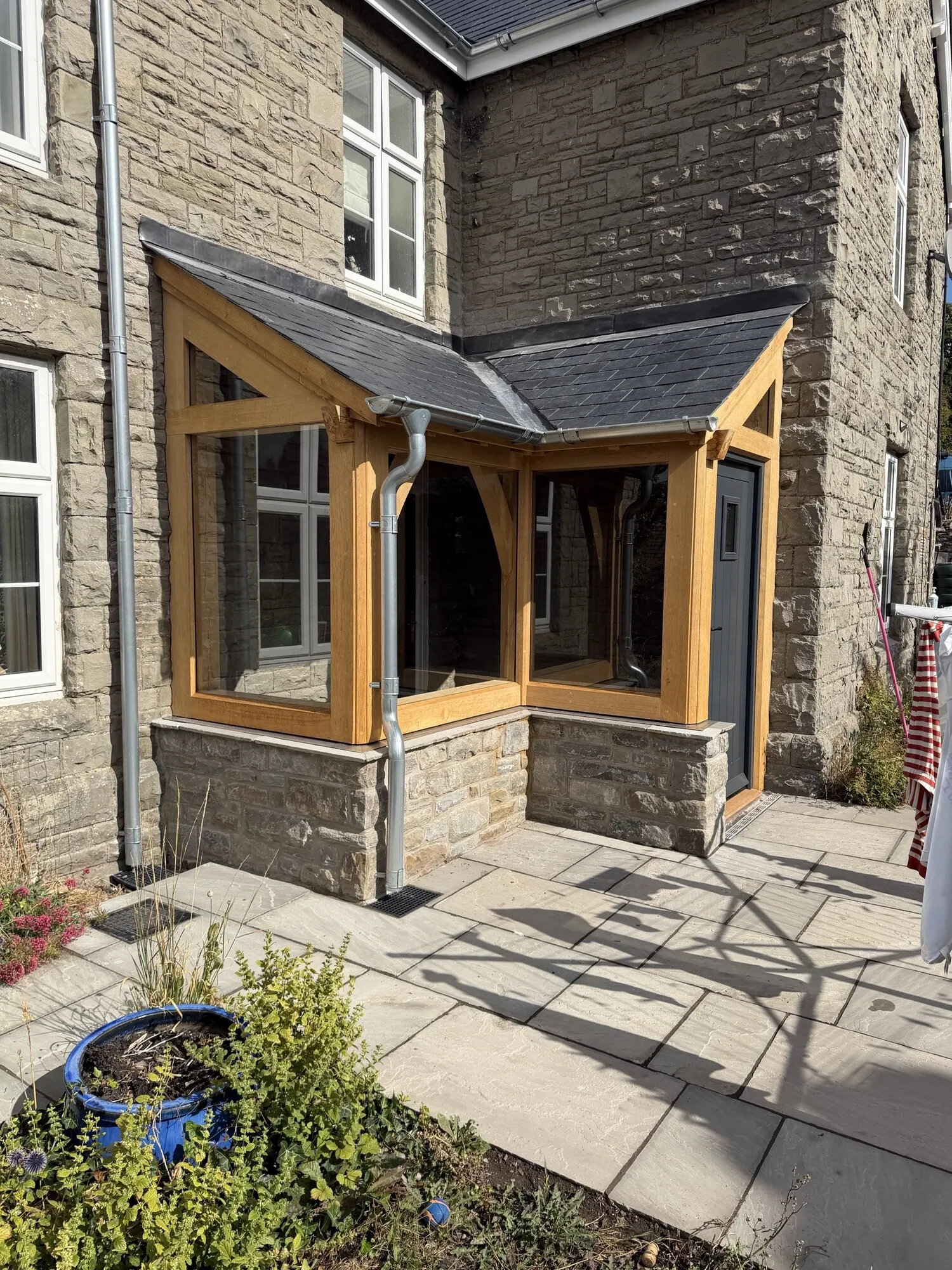 A glazed oak corner porch on its stone plinth against an old stone house in Crickhowell