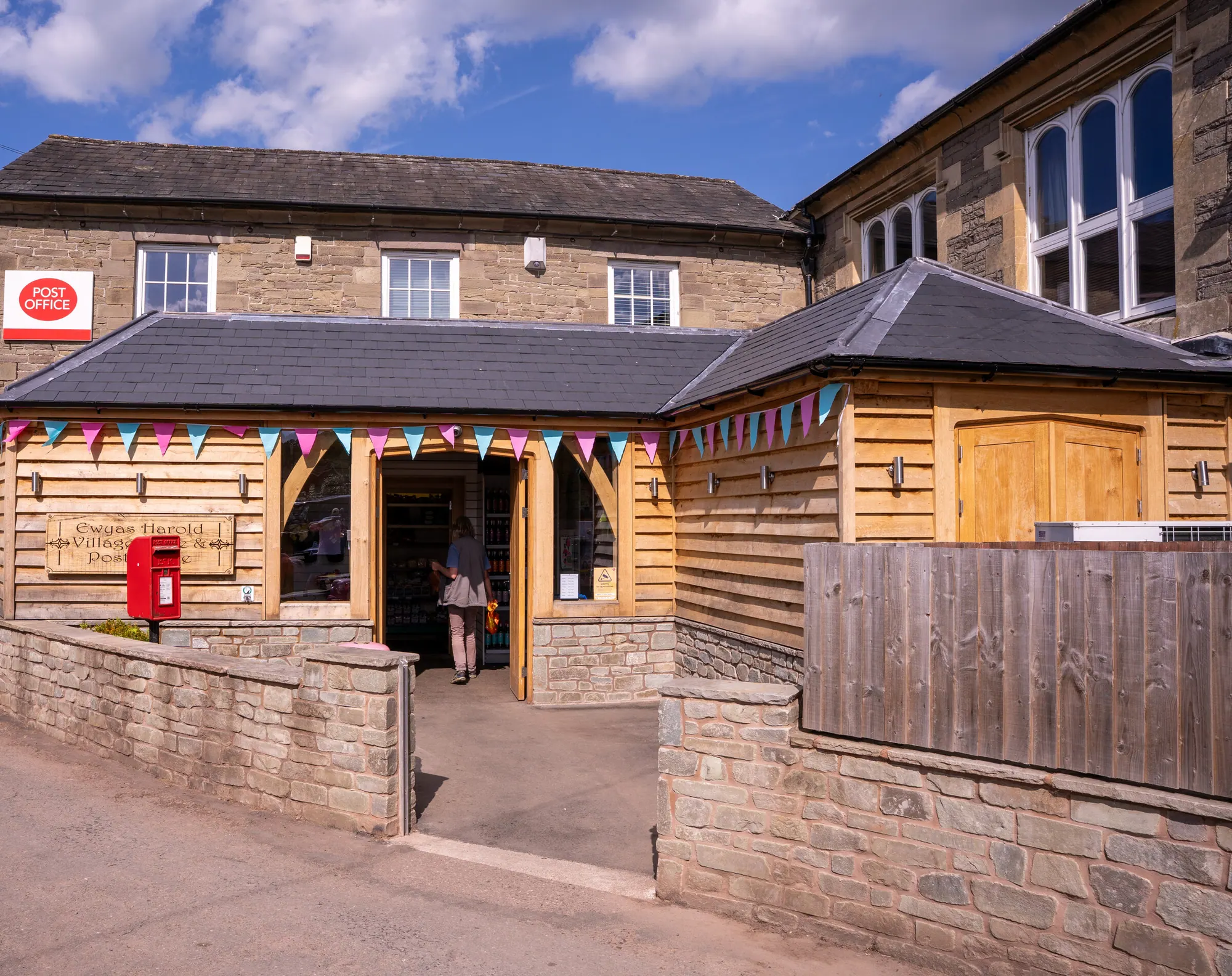 The oak frame extension across the front of Ewyas Harold village store and post office, oak cladding and a slate roof above a stone wall.