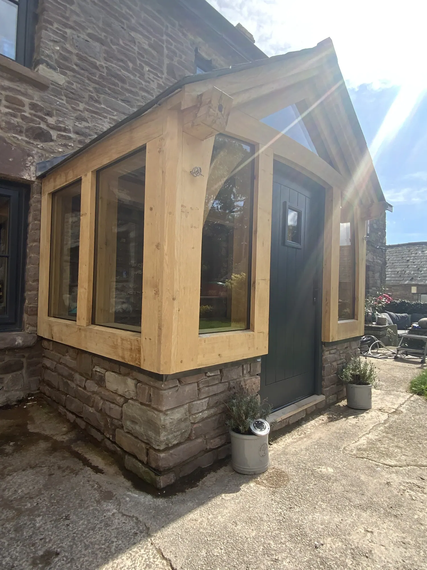 A glazed oak gable porch on its stone plinth at Llanbedr, seen from the corner