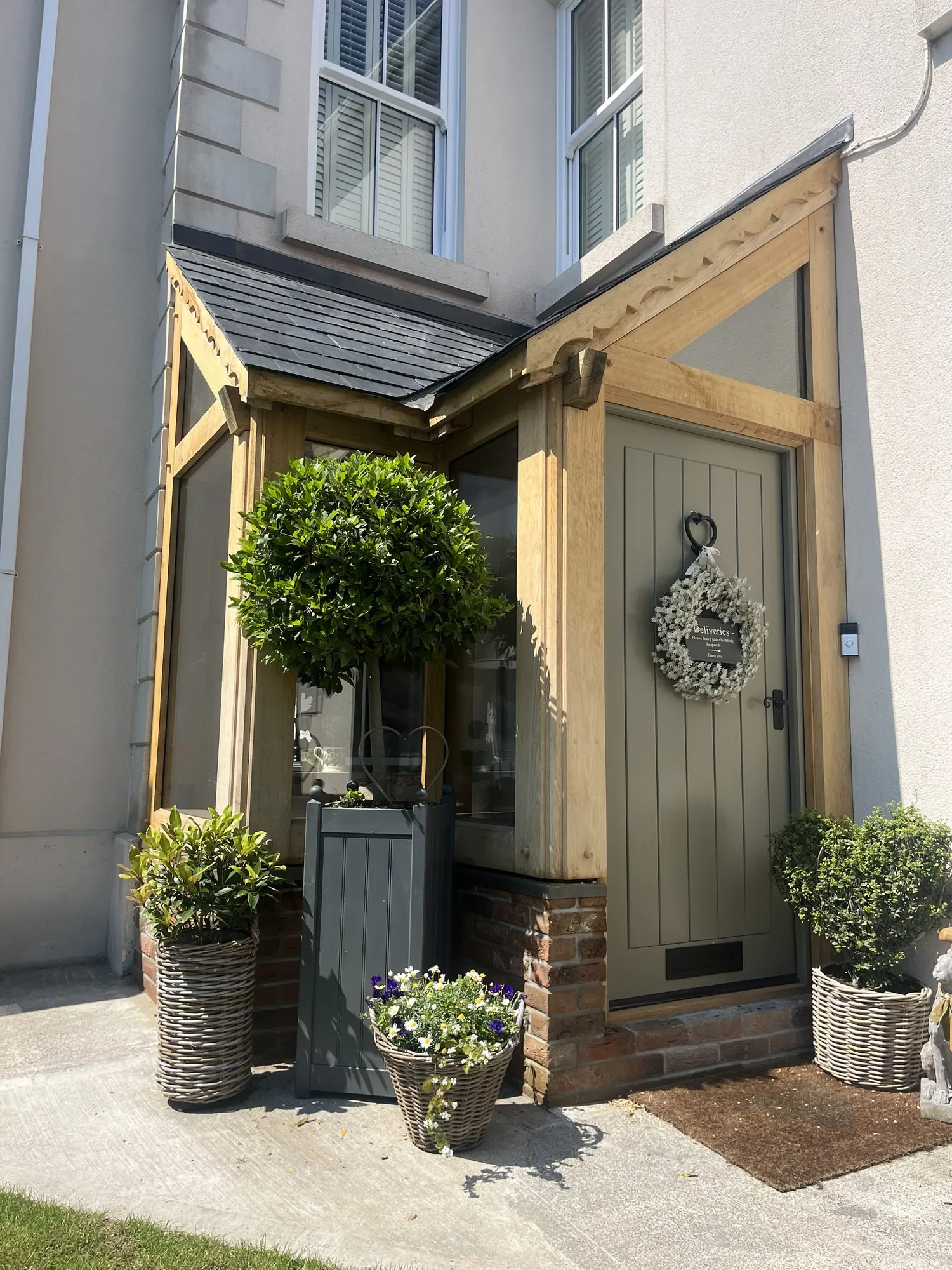 Glazed oak corner porch at Llandybie with a sage green door and planters