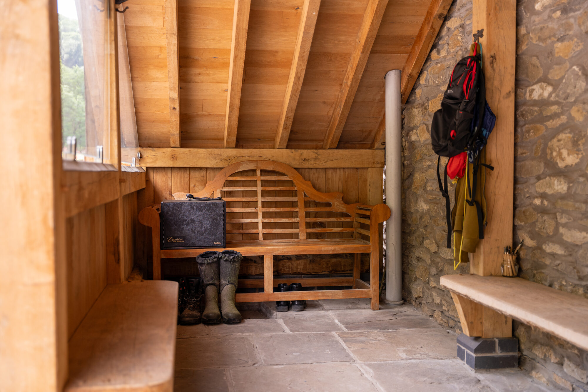 Inside an open oak porch near Usk: an oak bench, a flagstone floor and boots