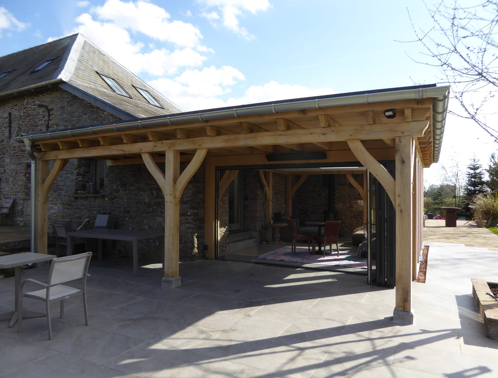 Flat-roofed oak frame living space against a stone barn at Llanvetherine, with bifold doors open onto the patio