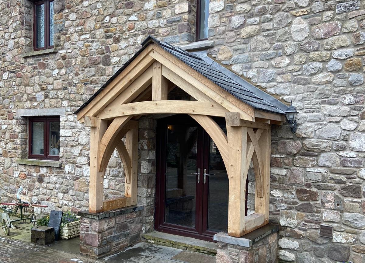Open oak porch on a converted stone barn at Raglan, with a curved tie, arched braces and jowl posts standing on stone plinths under a slate roof