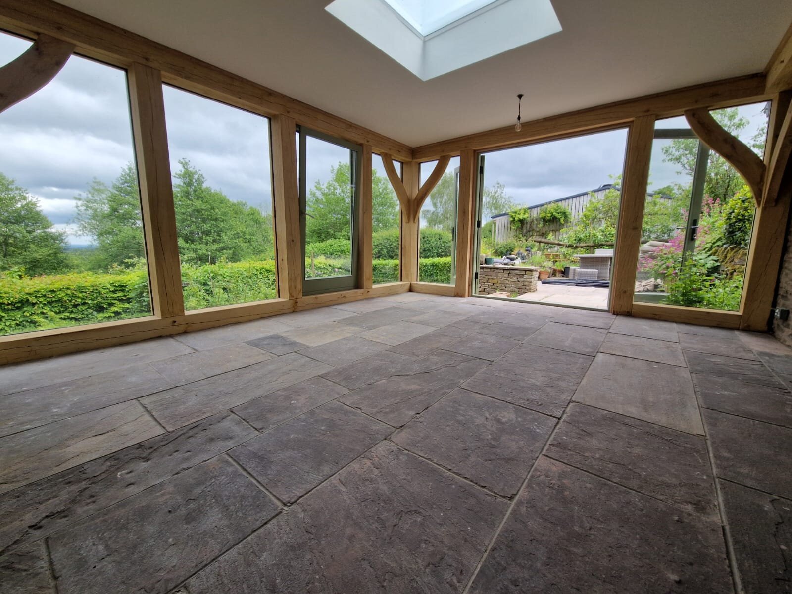 Inside the Longtown extension: floor-to-ceiling glazing on two sides, a rooflight set into the flat ceiling, and a stone flag floor