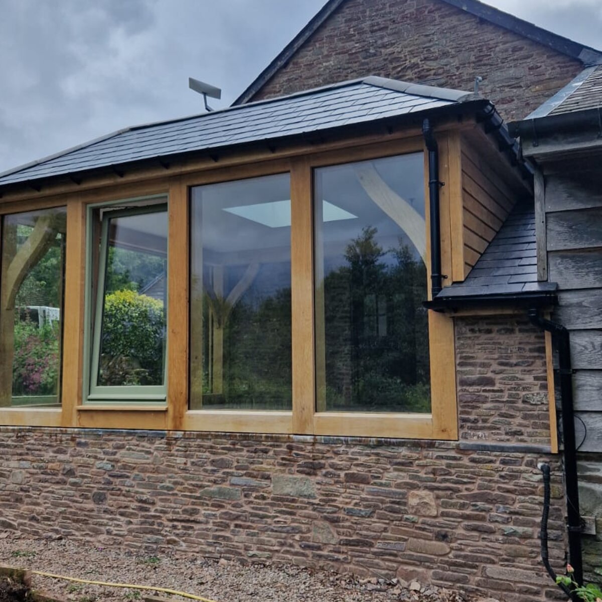 Oak frame extension with a hipped slate roof on a stone farmhouse at Longtown