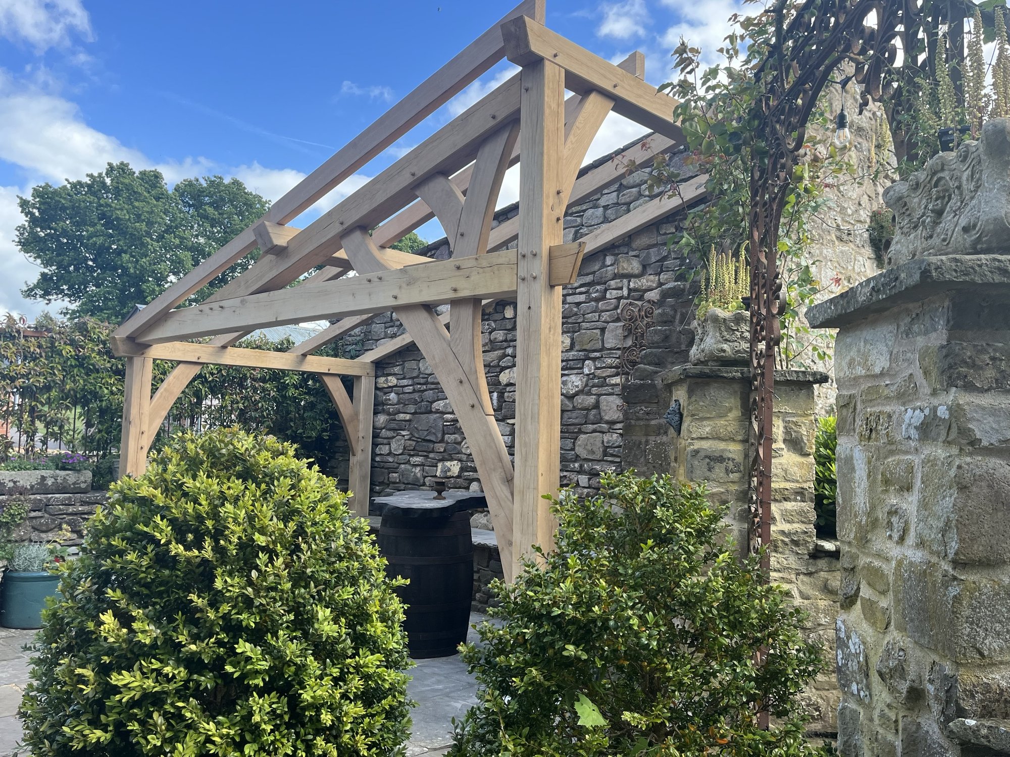 Oak lean-to shelter in the stone courtyard at Duffryn Mawr, Gilwern, with oak branch bracing and pegged joints set against an old stone wall