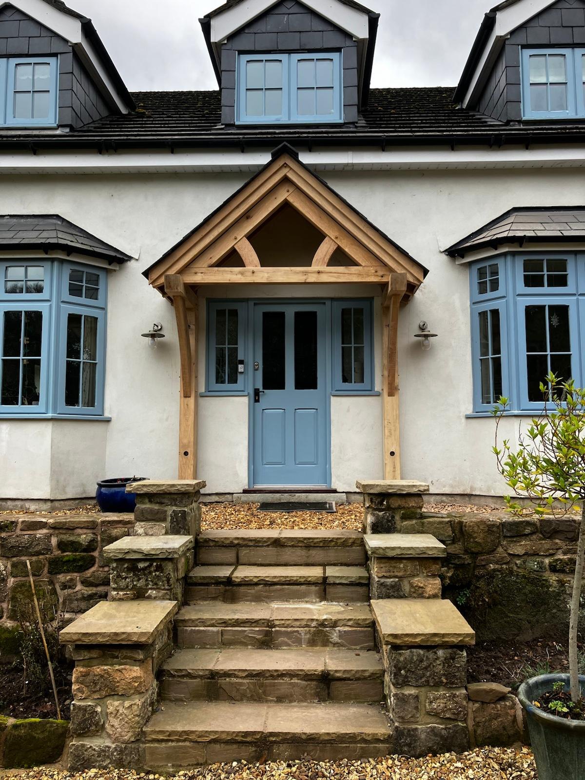 Cantilevered oak porch over a blue front door at the top of stone steps at Tintern