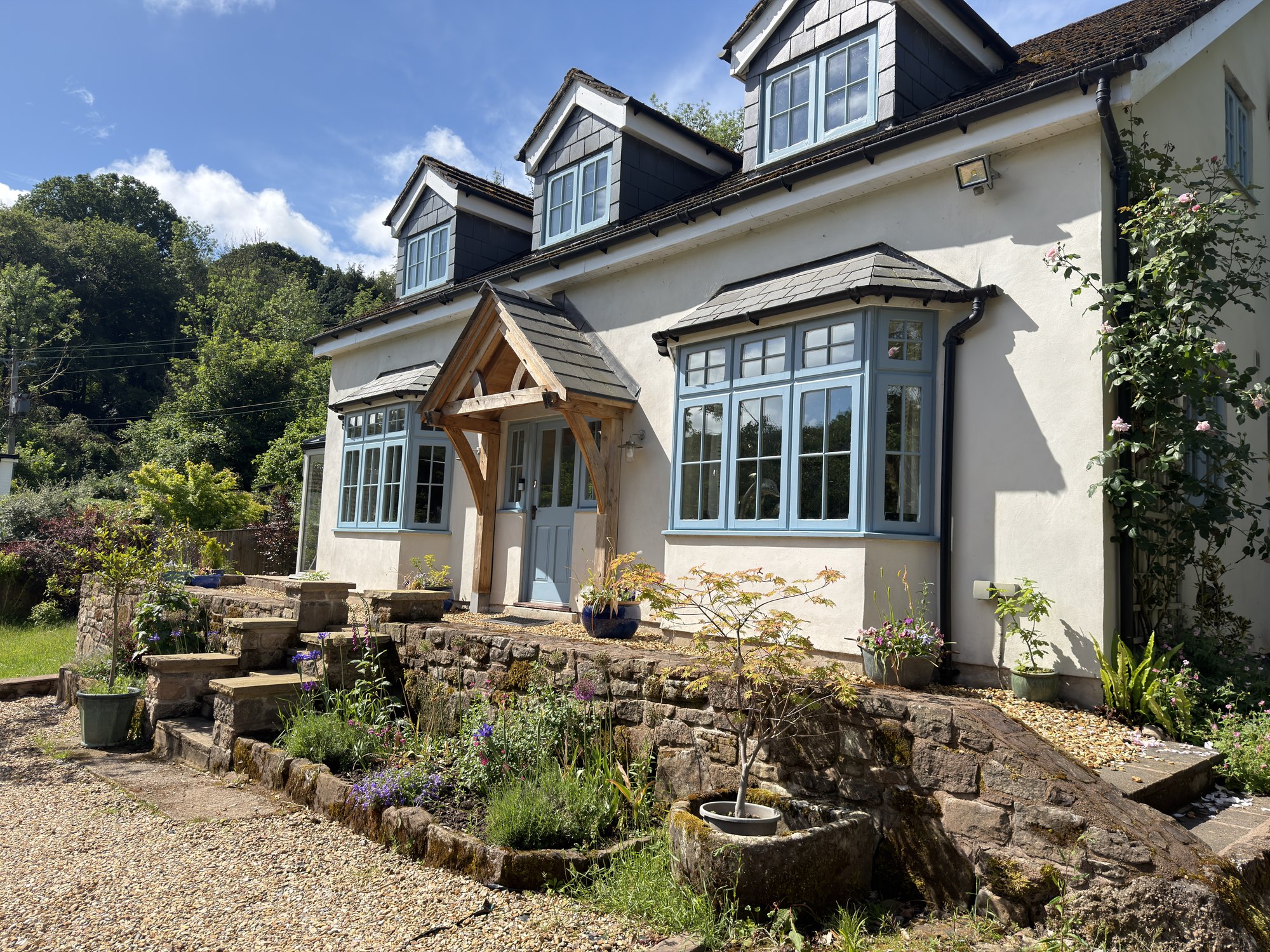 Cantilevered oak gable porch on a white cottage above a stone garden at Tintern
