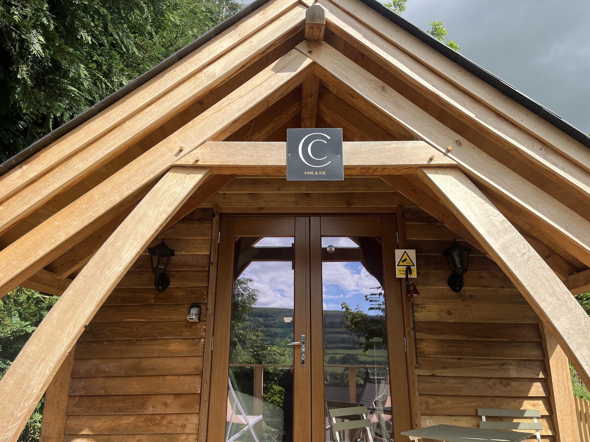Oak frame cabin at Cwmdu seen from the front, with its oak entrance porch, sling braces and glazed doors onto the deck