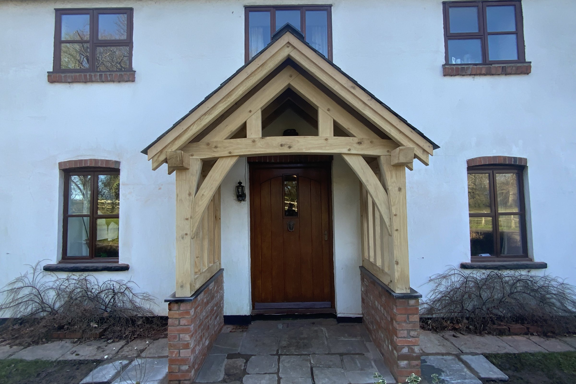Oak frame gable porch on red brick plinths across the front of a long white rendered farmhouse at Mamhilad