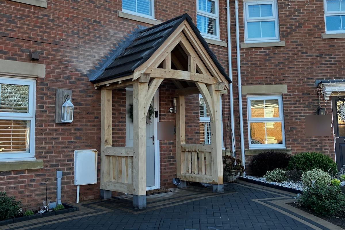 Oak frame gable porch with oak balustrade sides and a dark tiled roof on a red brick house at Pontllanfraith