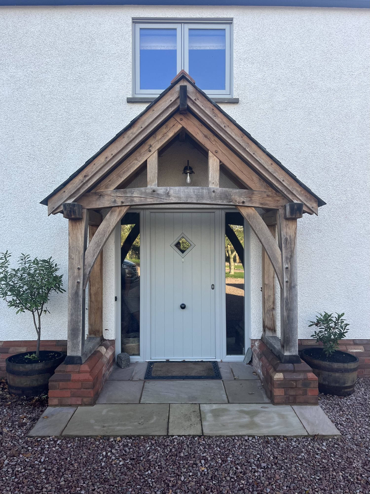 Straight-on view of a silvered oak gable porch on red brick plinths at Penpergwm